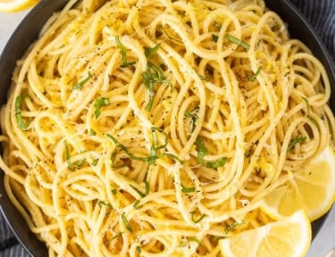 Lemon spaghetti plated with fresh chopped basil and lemon wedges on the side.
