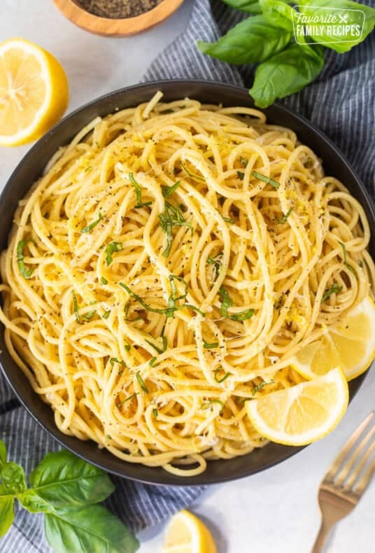 Lemon spaghetti plated with fresh chopped basil and lemon wedges on the side.