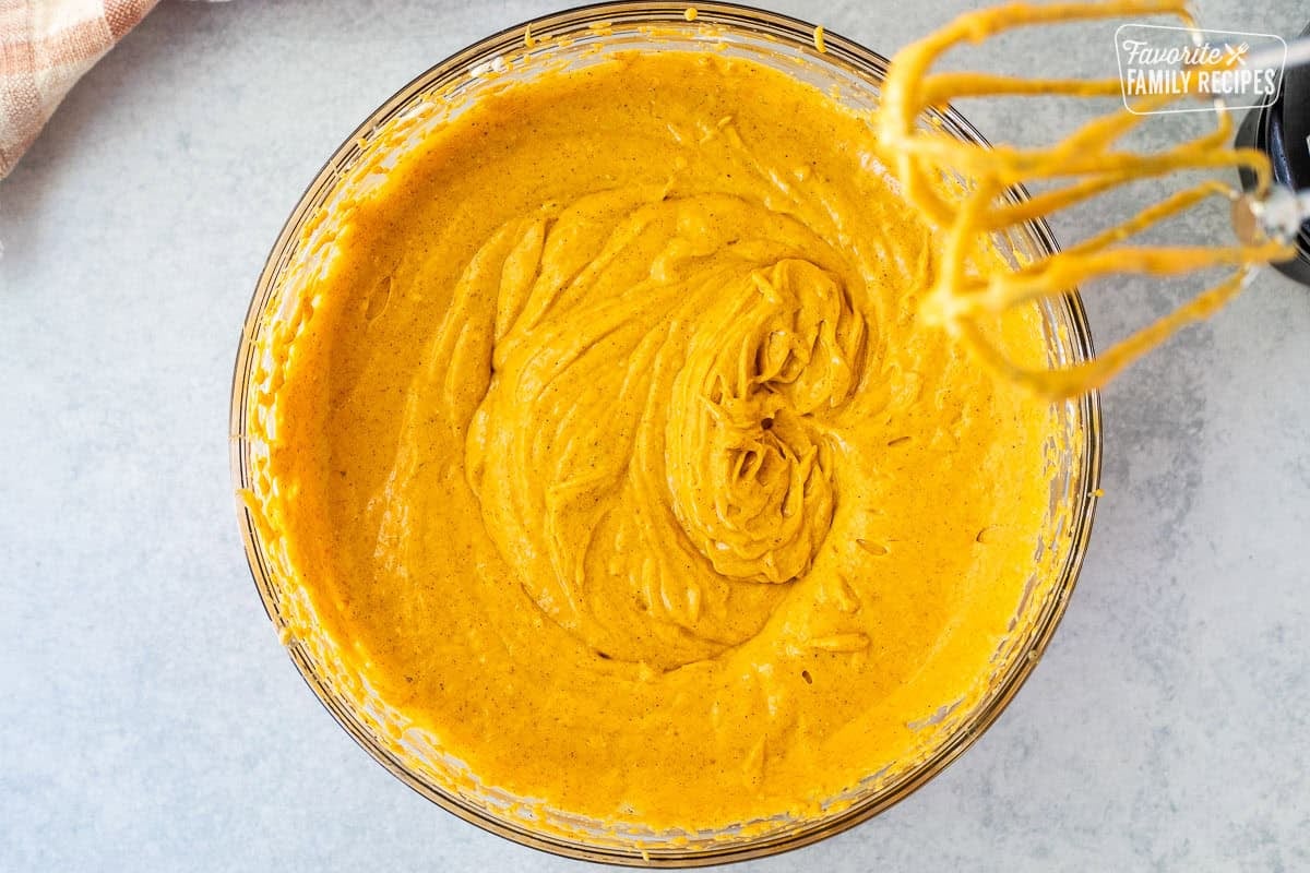 Glass mixing bowl with pumpkin mixture and electric mixers.
