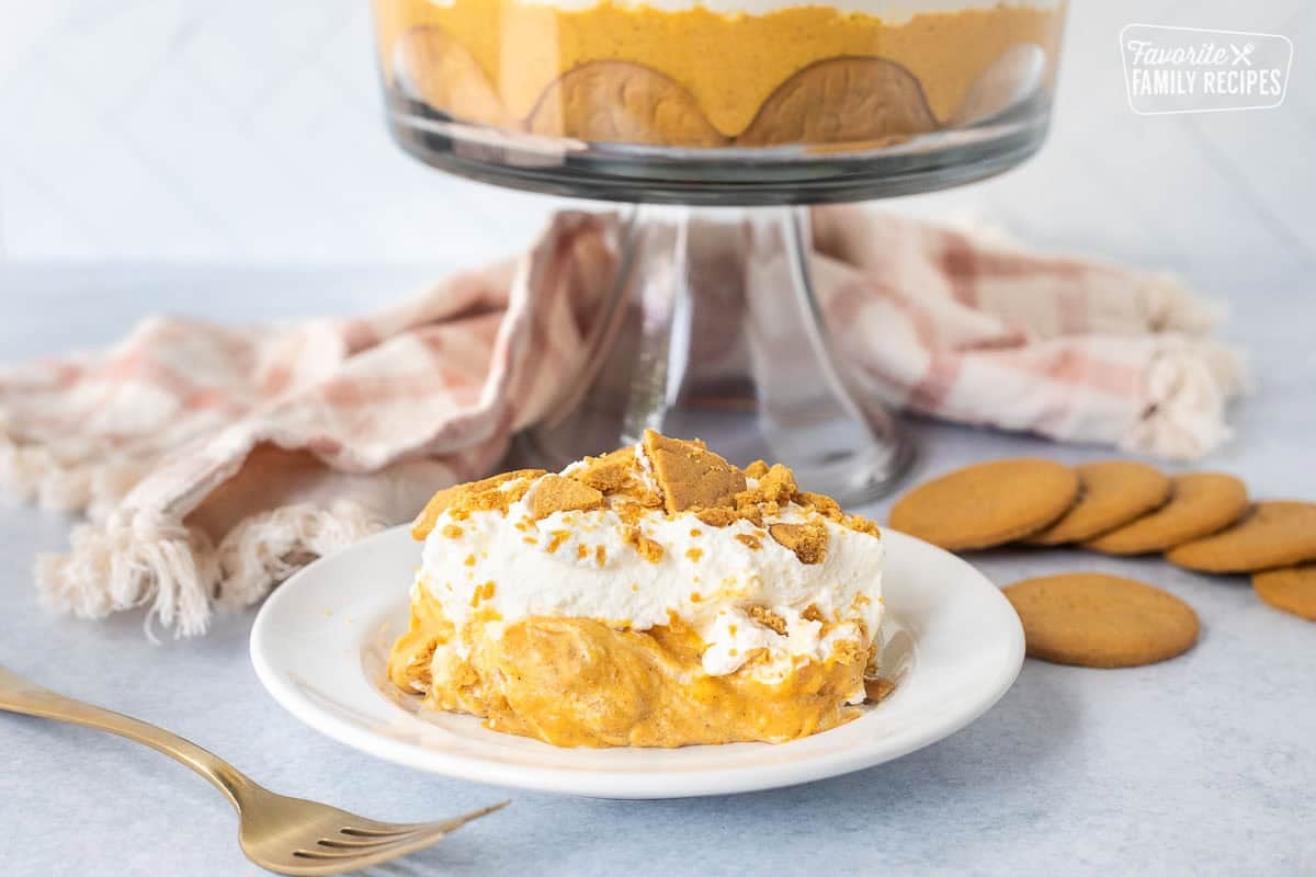 Serving of pumpkin trifle with ginger snap cookies, pumpkin cream cheese layer and whipped cream on a plate.