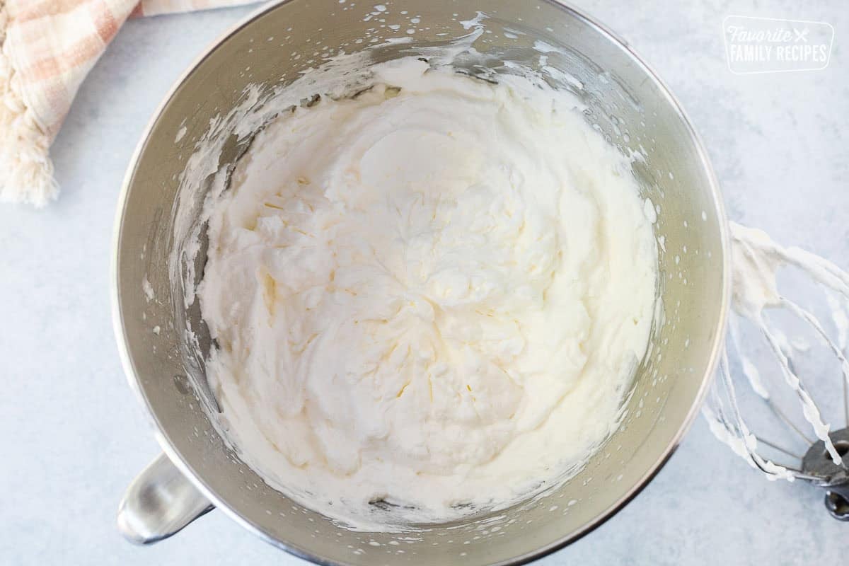Whipped cream in a mixing bowl with whisk attachment on the side.