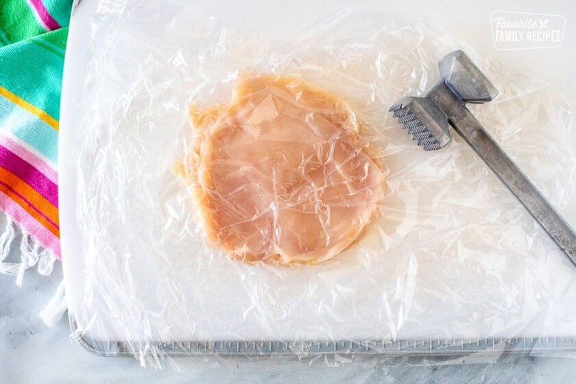 Pounding chicken breast between sheets of plastic wrap and a metal mallet.