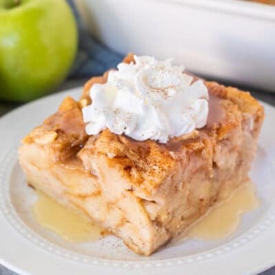 Slice of Apple Bread Pudding on a plate with caramel sauce and whipped cream.