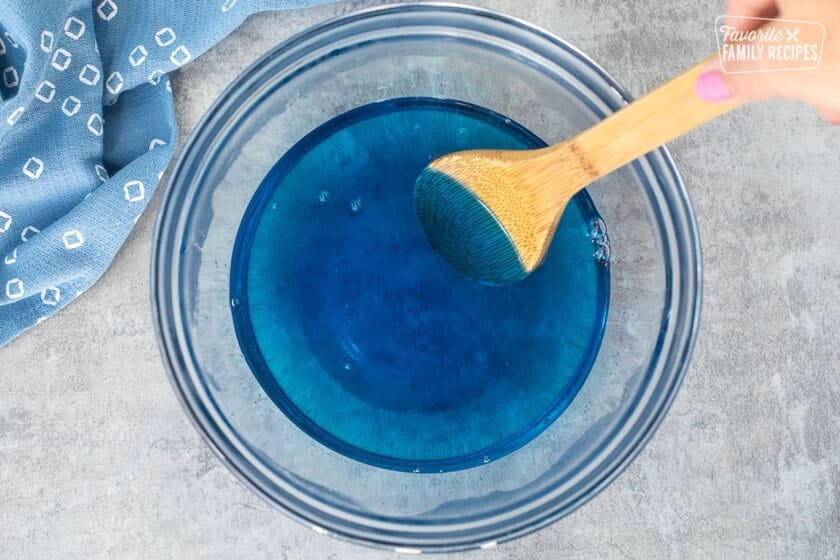 Mixing berry blue Jell-O in a bowl of hot water and a wooden spoon.