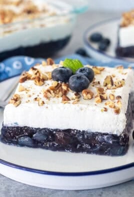 Slices of blueberry jello salad on a plate with pecans and fresh blueberries.