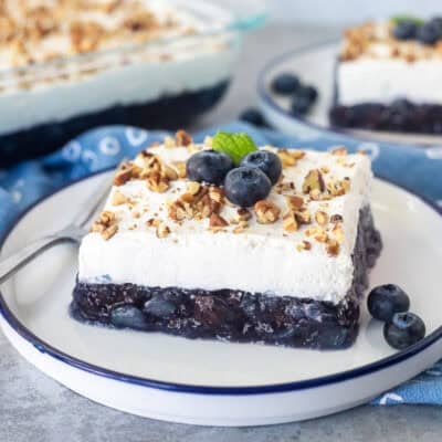 Slices of blueberry jello salad on a plate with pecans and fresh blueberries.