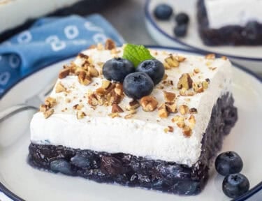 Slices of blueberry jello salad on a plate with pecans and fresh blueberries.