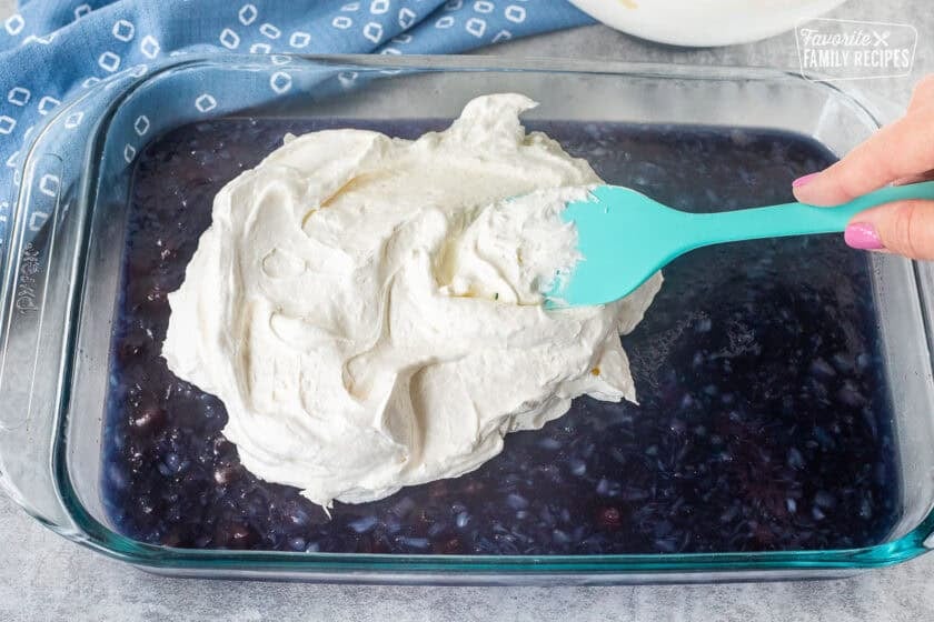 Spreading whipped topping on blueberry Jello salad in a glass dish.