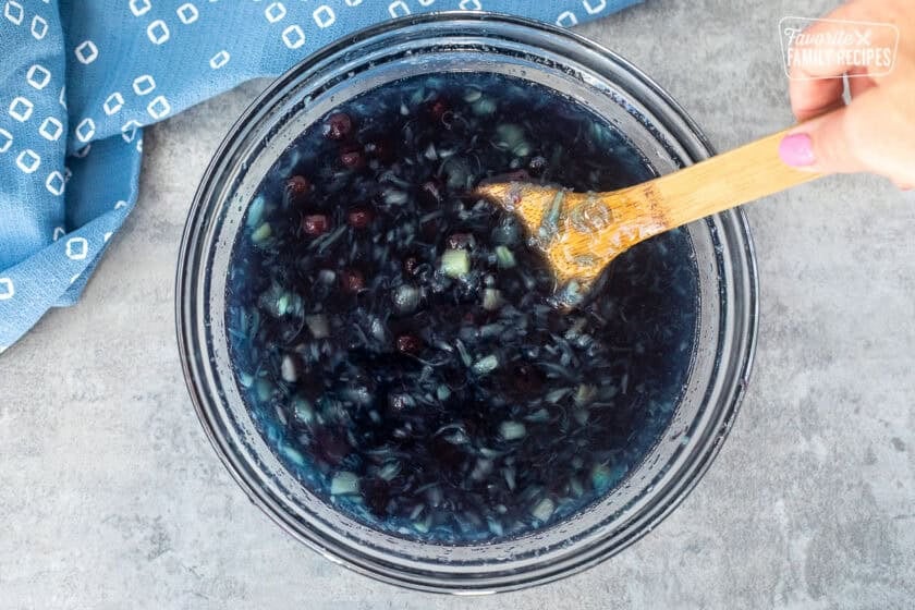 Mixing blueberry pie filling and crushed pineapple into glass bowl of berry blue Jell-O.