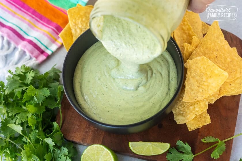 Pouring Cilantro Lime Sauce from mason jar into a bowl next to chips.