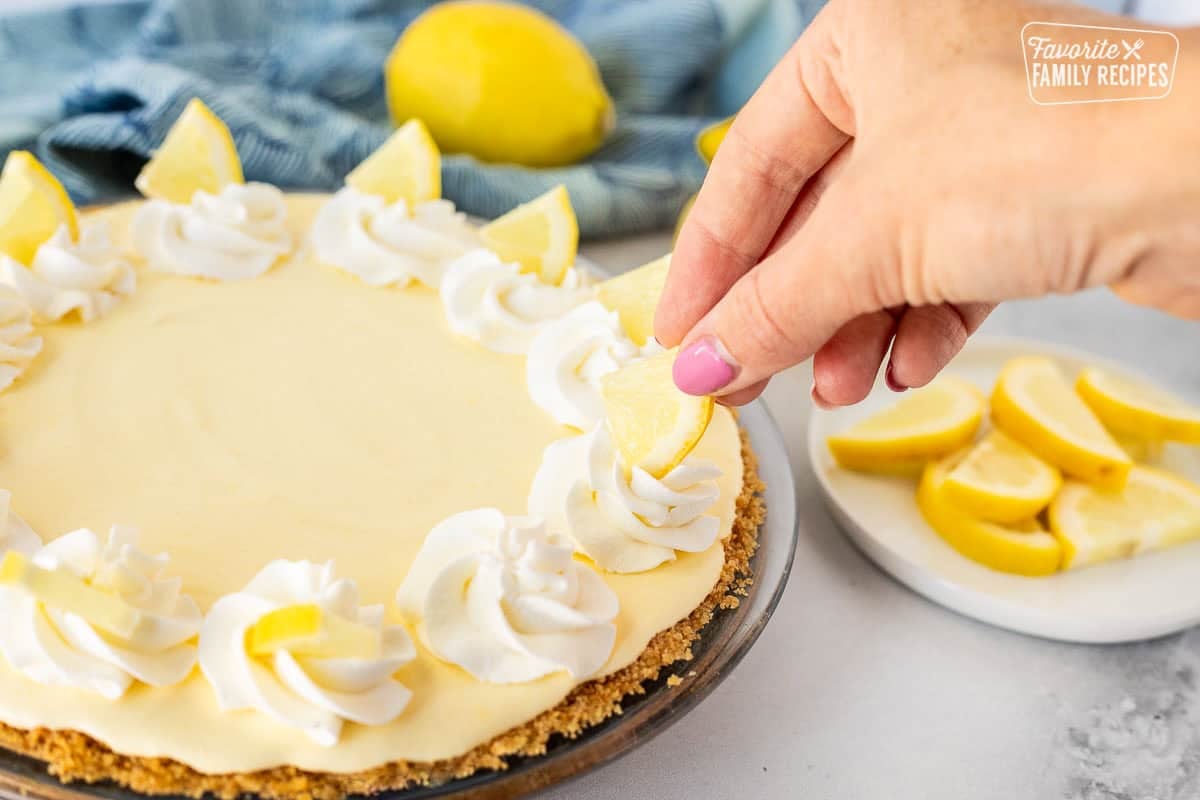 Decorating Creamy Lemon Pie with whipped cream and lemon slices.