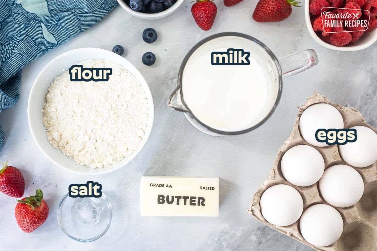 German pancakes recipe ingredients on a countertop: flour, milk, eggs, butter, salt, and fresh fruit