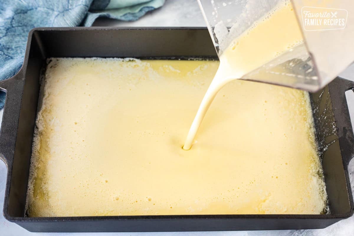 Pouring German pancake batter from blender into baking dish.