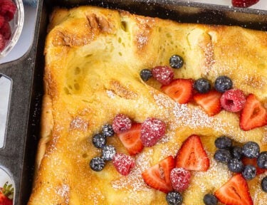 German pancakes in a baking dish topped with powdered sugar, sliced strawberries, raspberries and blueberries.