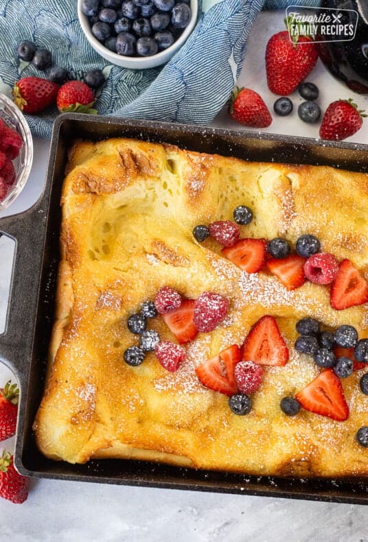 German pancakes in a baking dish topped with powdered sugar, sliced strawberries, raspberries and blueberries.