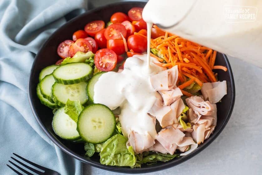 Pouring homemade ranch from a glass pitcher onto a chef salad.