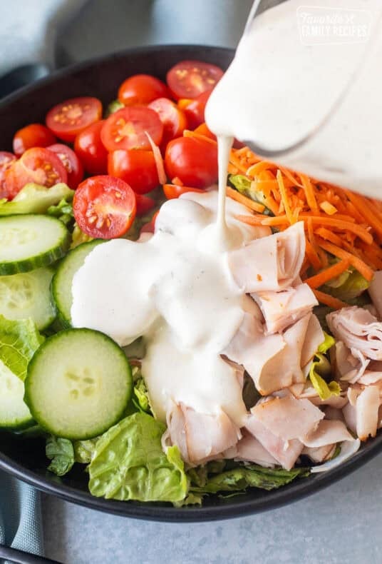 Pouring homemade ranch from a glass pitcher onto a chef salad.