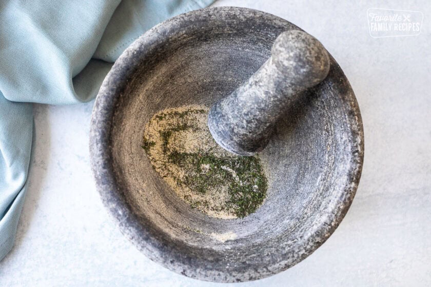 Stone mixing bowl with spices and herbs for homemade ranch recipe.