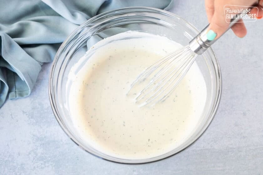 Glass mixing bowl with whisk mixing homemade ranch recipe.
