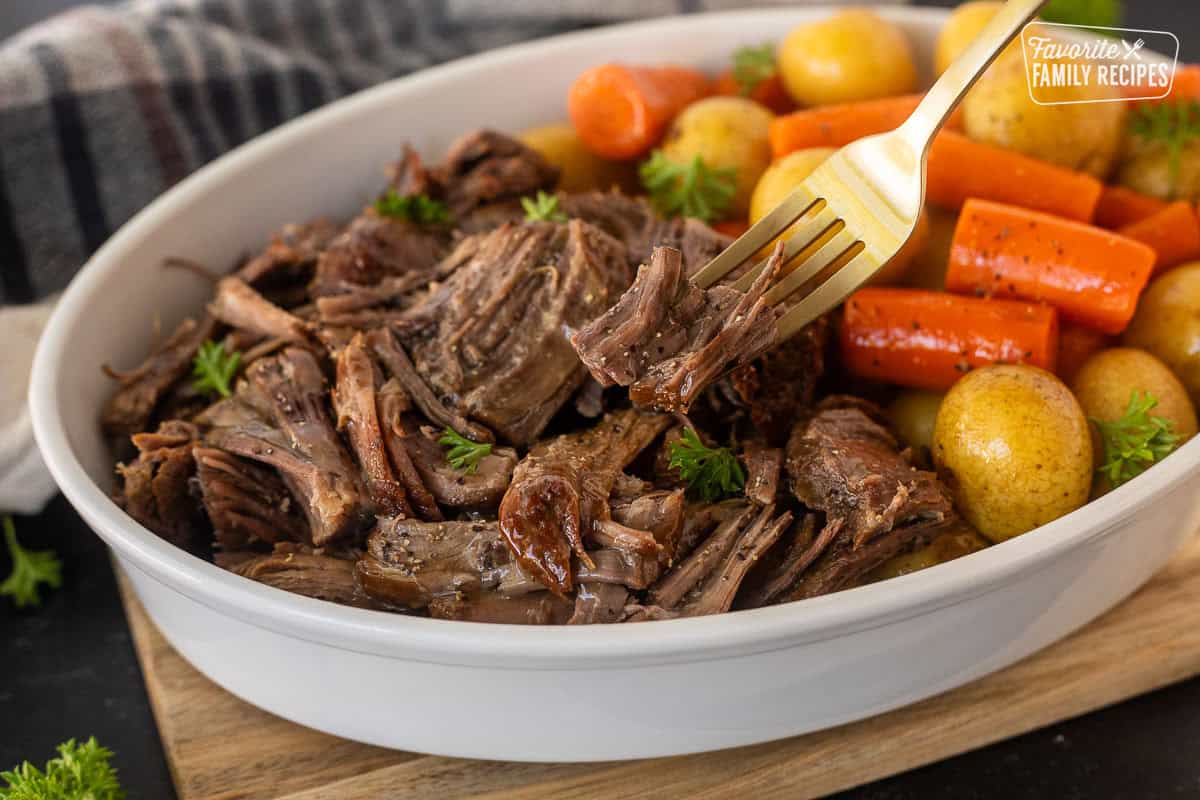 Instant pot chuck roast shredded in dish and piece on fork. Cooked carrots and baby potatoes also in dish.