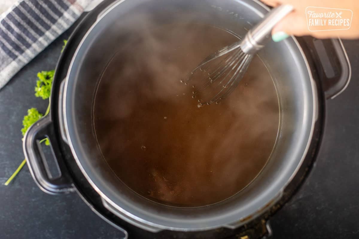 Stirring cornstarch slurry into beef drippings in instant pot with whisk.