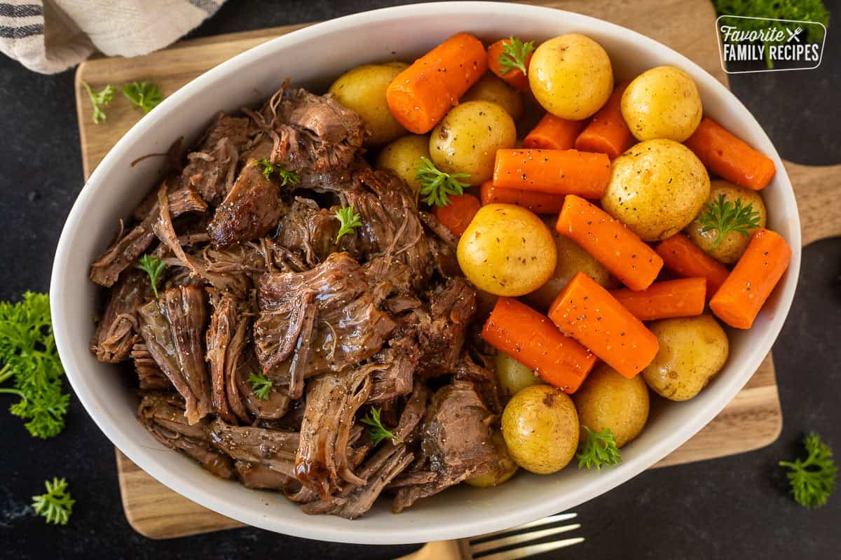Oval dish with shredded instant pot chuck roast next to cooked carrots and potatoes.
