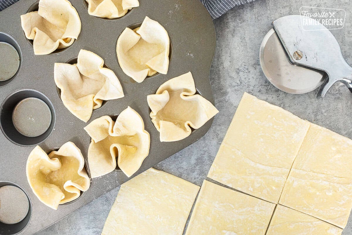 Cut puff pastry with pizza cutter and muffin dish with pastry pieces.