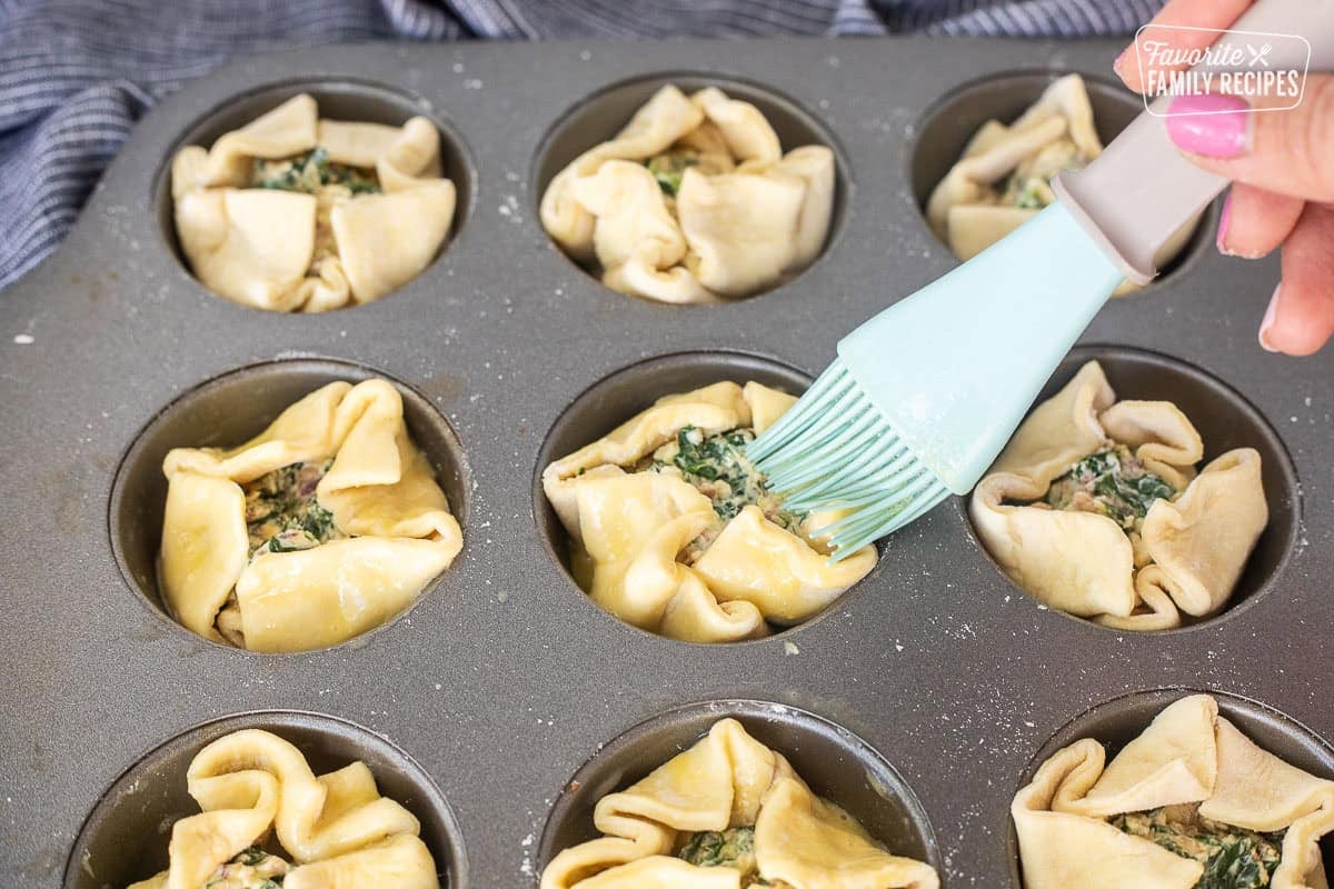 Brushing egg wash on top of puff pastry filled with spinach mixture.