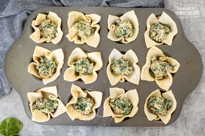 Muffin pan with cut pieces of puff pastry filled with spinach mixture.