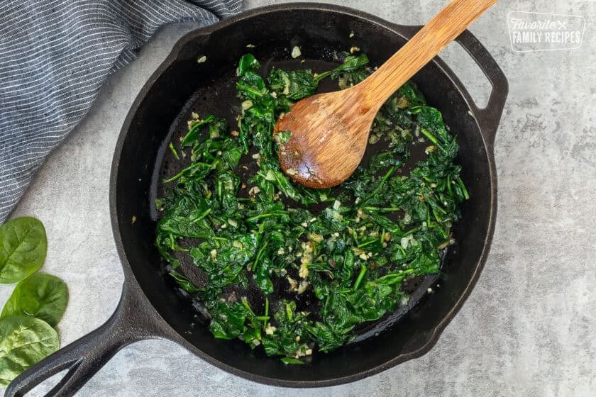 Skillet with spinach and garlic and a wooden spoon.