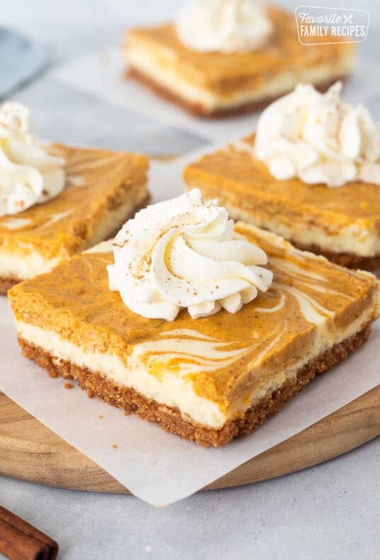Pumpkin cheesecake bars topped with whipped cream and cinnamon.