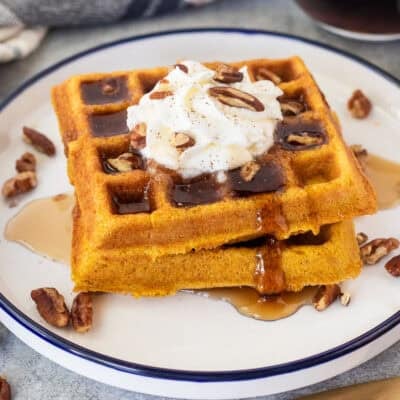 Maple syrup on stacked pumpkin waffles with whipped cream and pecans.