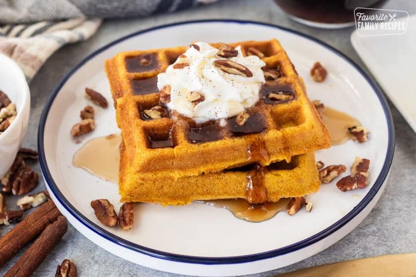 Maple syrup on stacked pumpkin waffles with whipped cream and pecans.