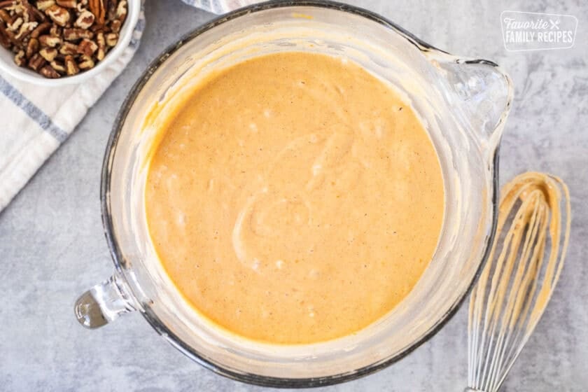 Glass mixing bowl with pumpkin waffle batter and whisk on the side.
