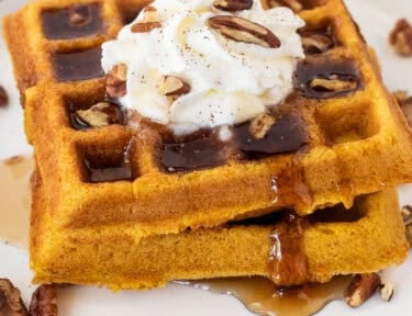 Maple syrup on stacked pumpkin waffles with whipped cream and pecans.