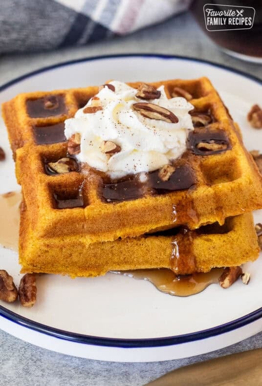 Maple syrup on stacked pumpkin waffles with whipped cream and pecans.