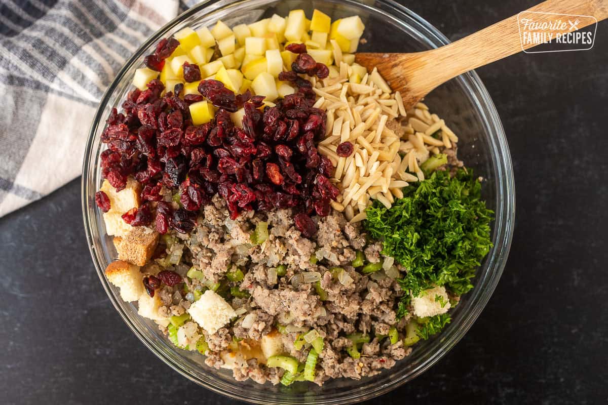 Glass bowl of bread, slivered almonds, parsley, craisins, golden delicious apples and sausage mixture.
