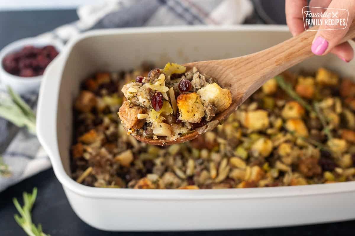 Sausage stuffing in a wooden spoon over baking dish.