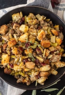 Sausage Stuffing in a bowl garnished with thyme and a wooden spoon of sausage stuffing.