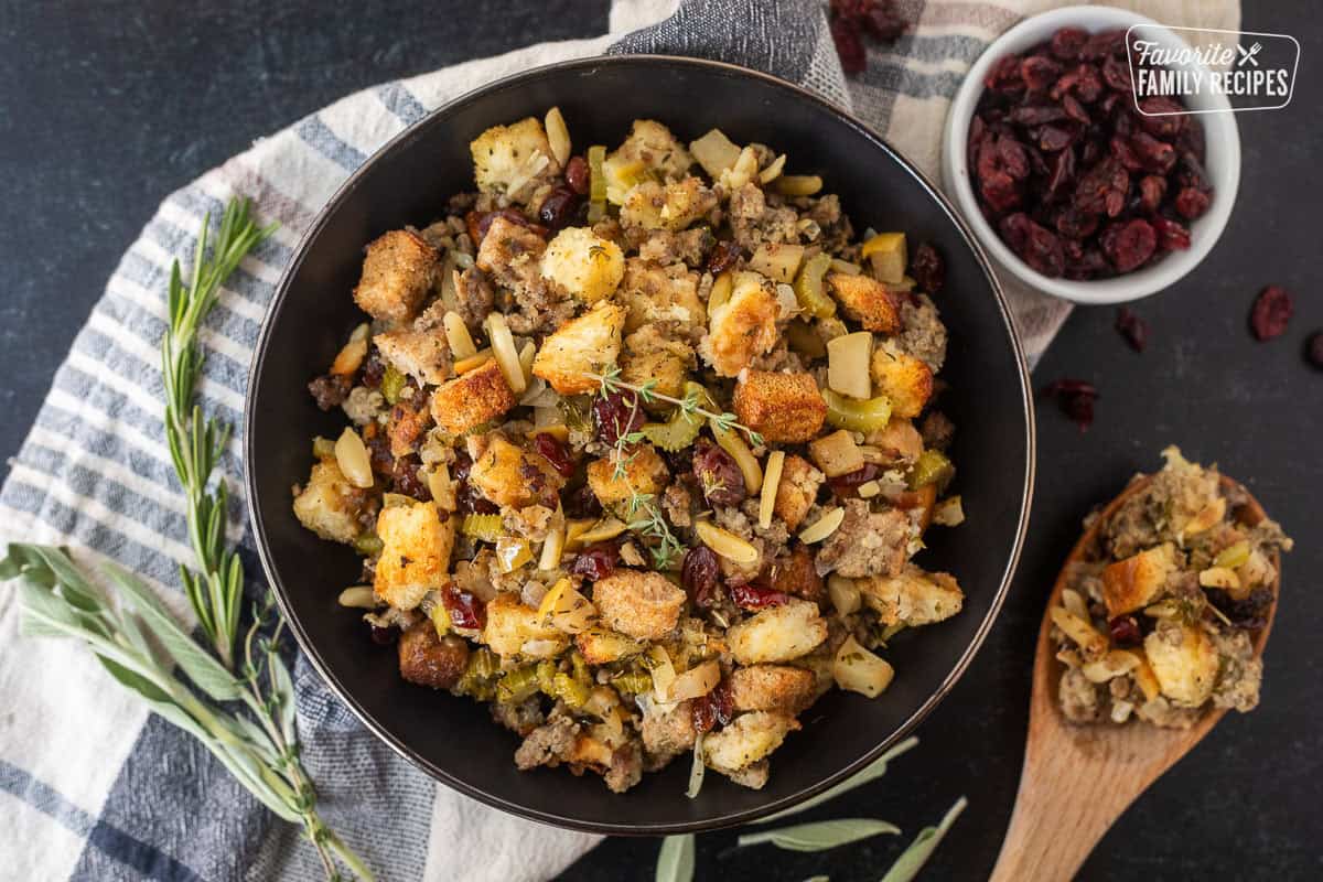 Cranberry Sausage Stuffing is every festive flavor of Thanksgiving baked into one savory, sweet and very satisfying dish. You'll love the cranberries, apples, sausage and herbs in each bite. Sausage Stuffing in a bowl garnished with thyme and a wooden spoon of sausage stuffing.