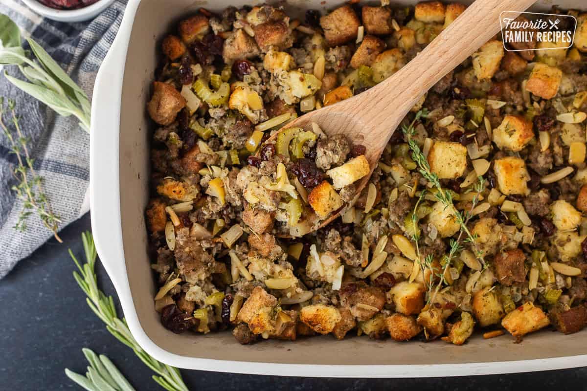 Sausage Stuffing has every festive flavor of Thanksgiving baked into one savory, sweet, and very satisfying dish. You'll love the cranberries, apples, sausage, and fresh herbs in each bite. Glass baking dish of Sausage stuffing and wooden spoon.