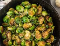 Skillet with Sautéed Brussels Sprouts garnished with shredded parmesan cheese.