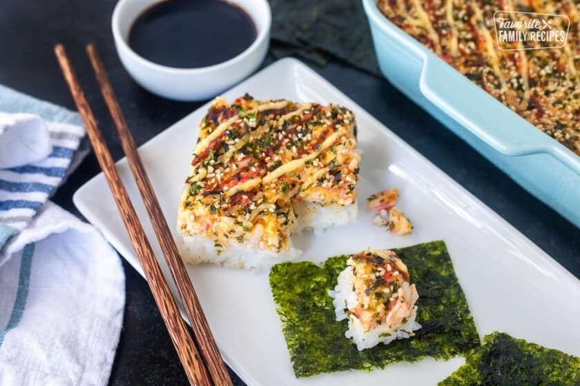 Sushi Bake slice on plate with Nori squares and chop sticks.