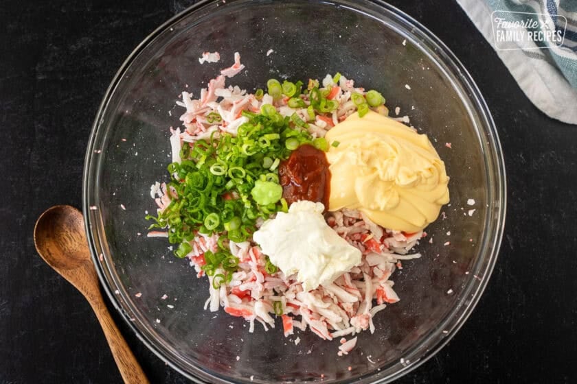 Glass bowl with imitation crab, mayo, cream cheese, Sriracha sauce, wasabi, and green onion for sushi casserole layer.