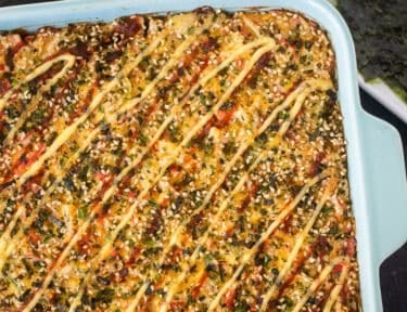 Sushi Bake in a casserole dish with soy sauce and nori on the side.