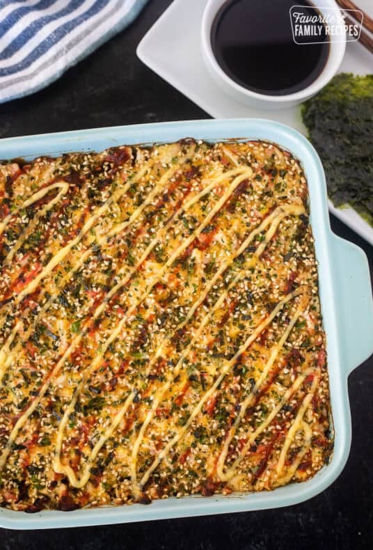 Sushi Bake in a casserole dish with soy sauce and nori on the side.