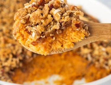 Sweet Potato Casserole with Pecan Topping on a serving wooden spoon over a baking dish.