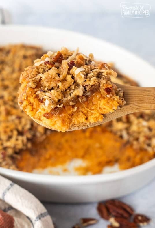 Sweet Potato Casserole with Pecan Topping on a serving wooden spoon over a baking dish.