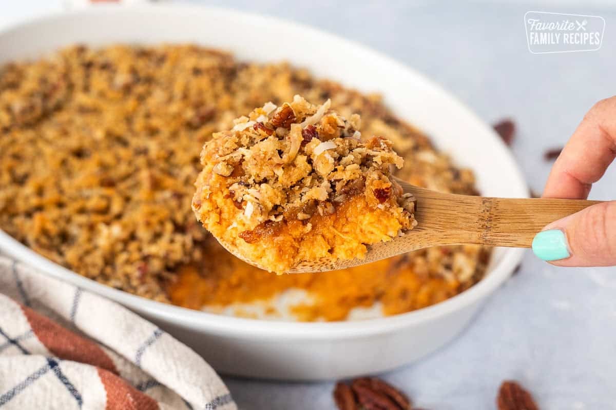 Sweet Potato Casserole with Pecan Topping on a serving wooden spoon over a baking dish.