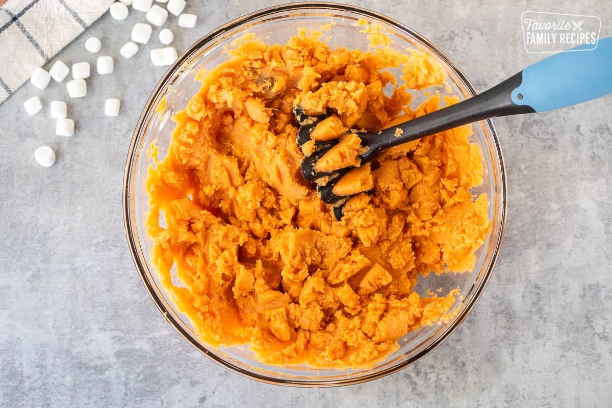 Glass bowl with smashed sweet potatoes and masher.